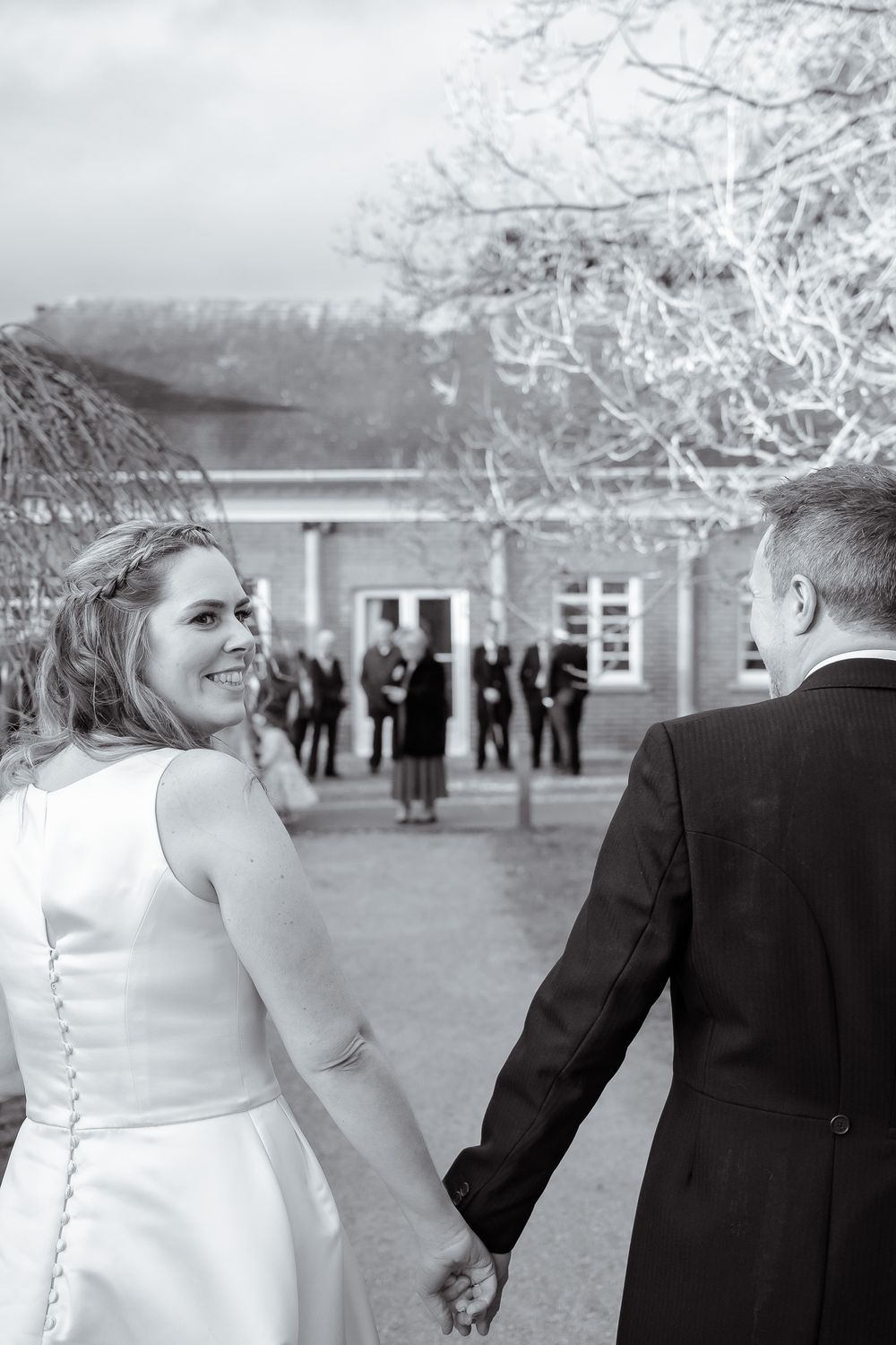 A candid wedding moment captured in black and white as guests gather in the background.