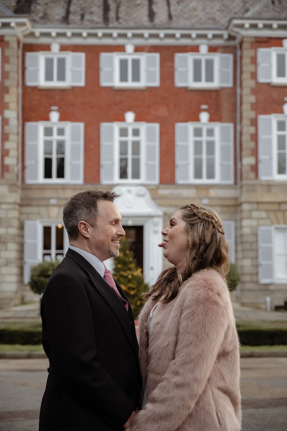 A couple shares a joyful moment outside a historic red brick building with white shutters.