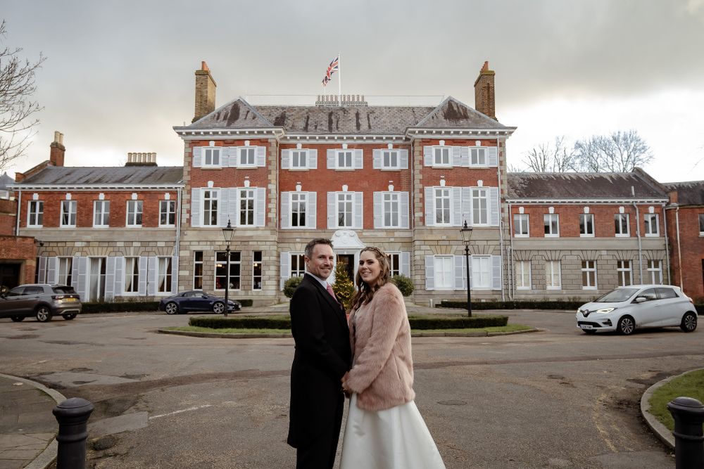 A wedding couple poses in front of a grand red brick mansion on their special day.