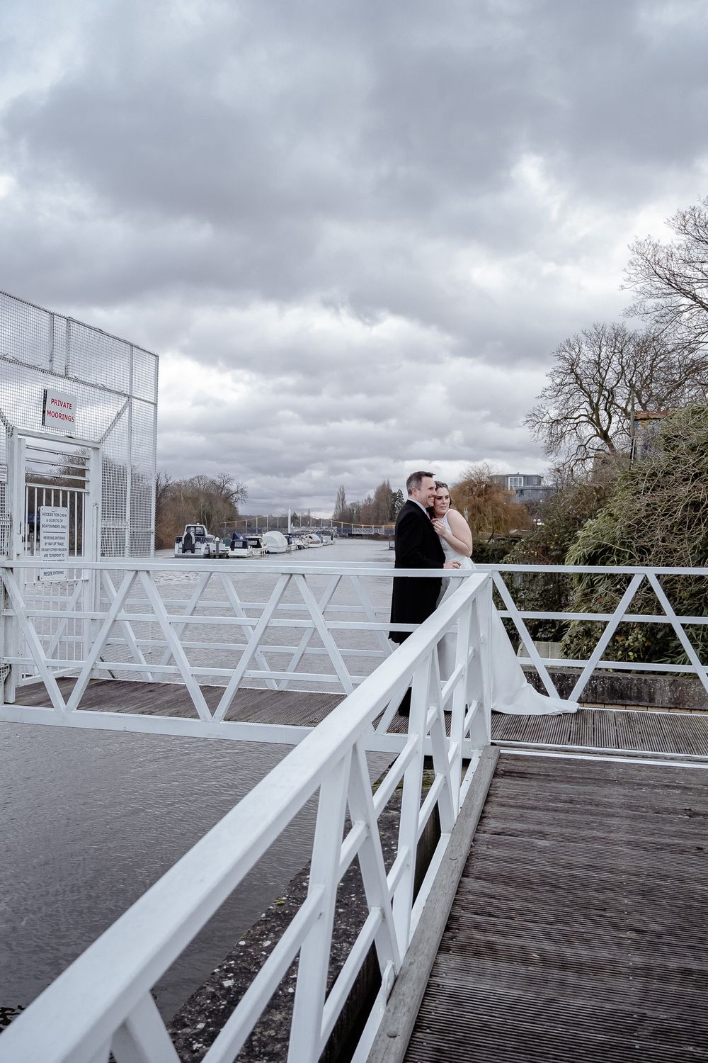 A wedding couple shares a tender moment on a white boardwalk with cloudy skies above.