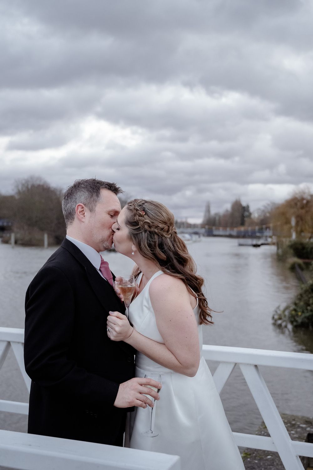 A romantic moment between newlyweds on a white bridge overlooking a river.