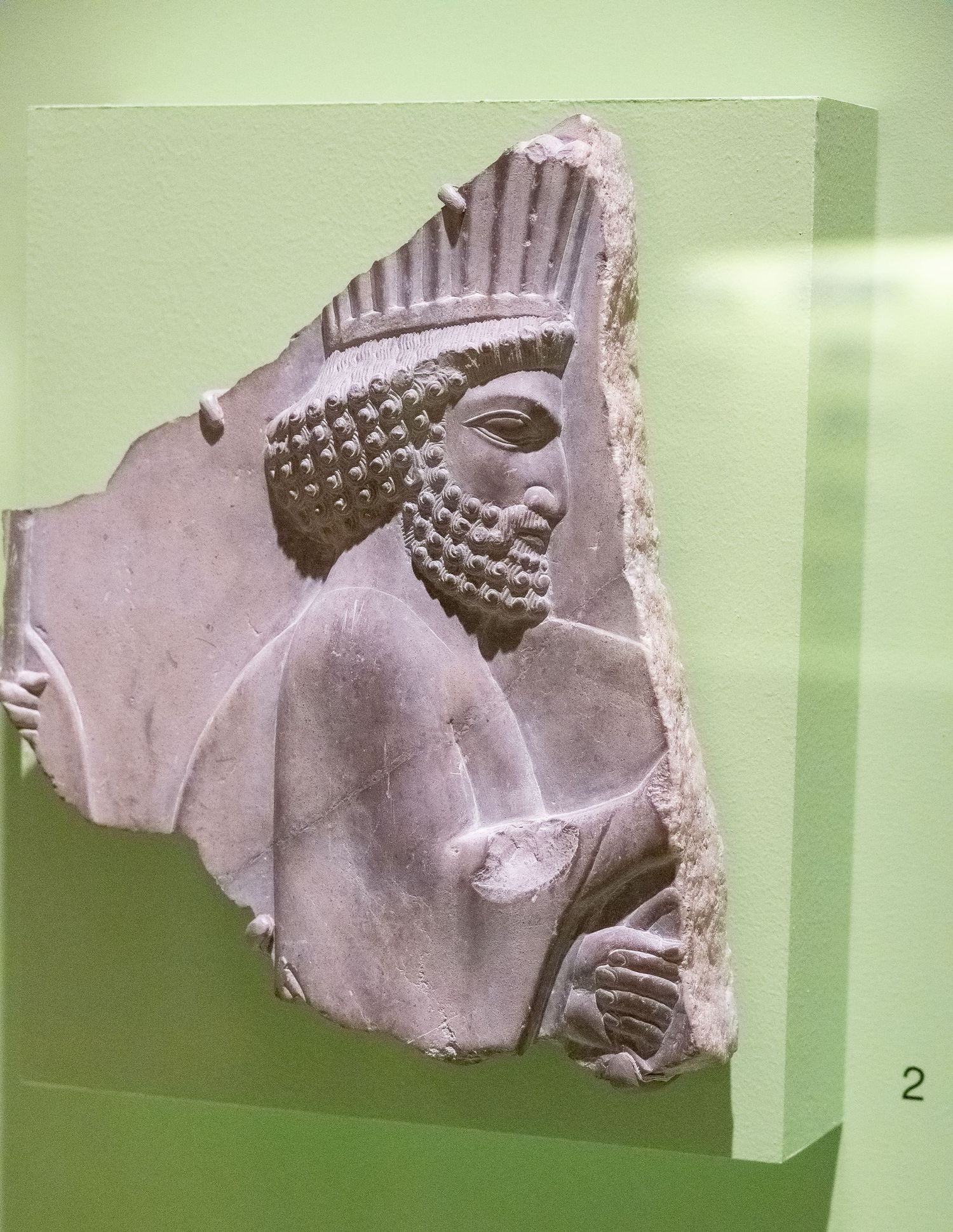 Carved stone relief fragment showing a bearded figure in Persian or Mesopotamian style.