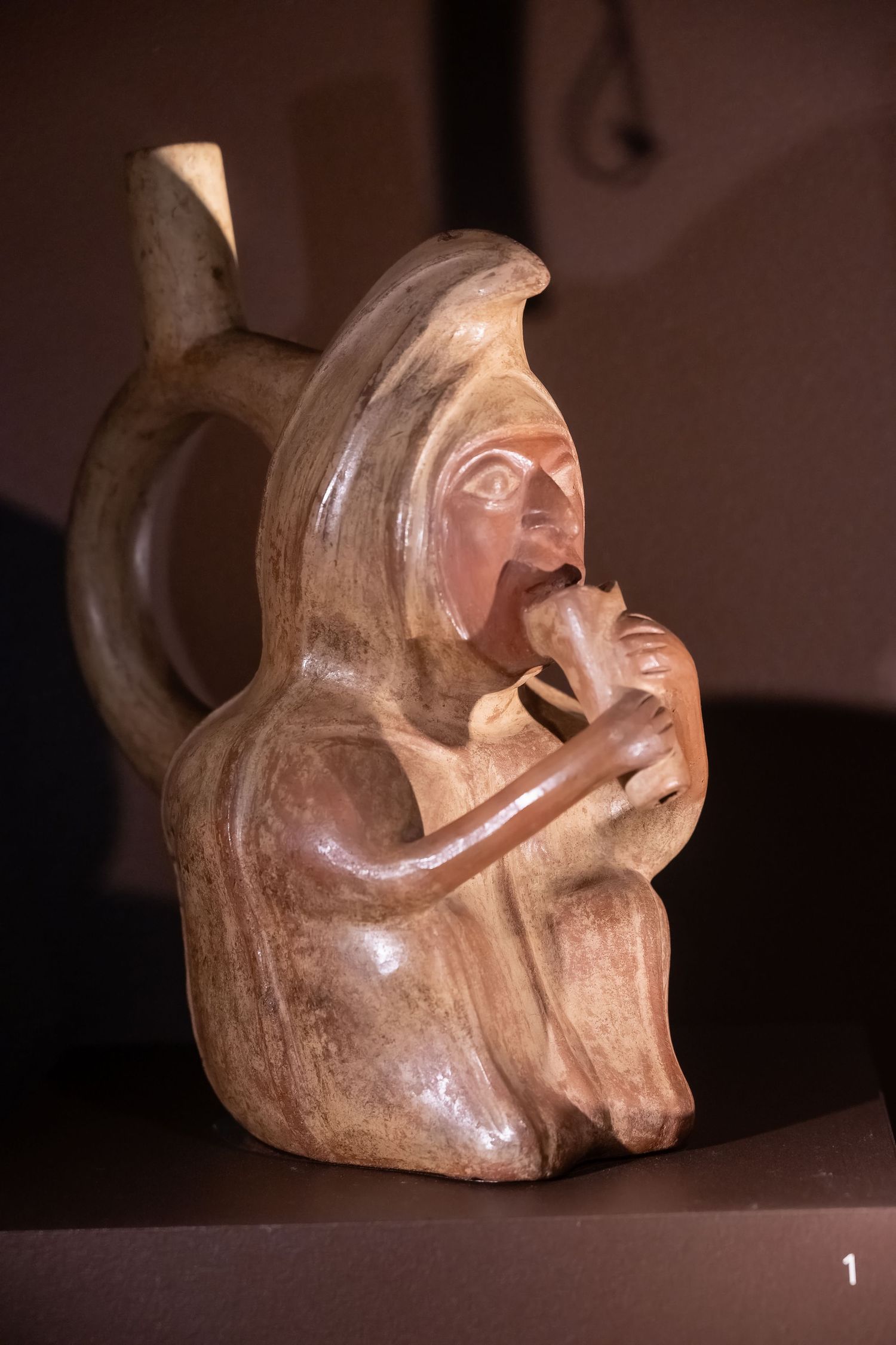 Pre-Columbian ceramic vessel shaped like a seated figure playing a musical instrument.