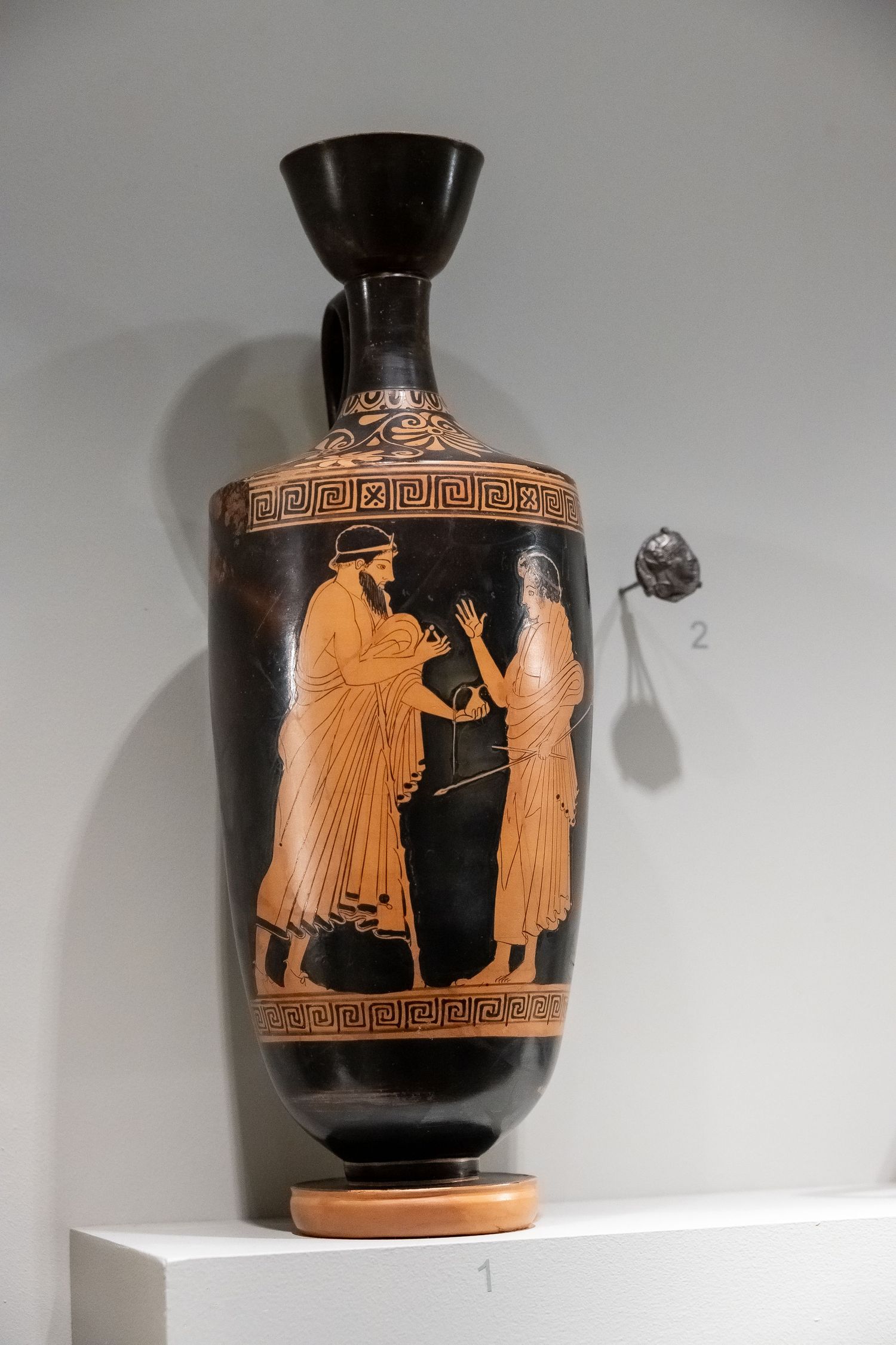 Ancient Greek lekythos vase with black and orange figures depicting a classical scene with geometric patterns.