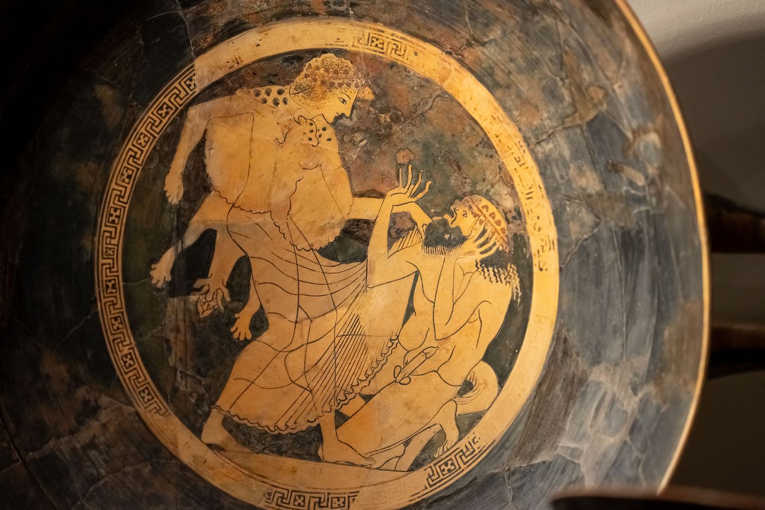 Ancient Greek pottery plate showing mythological scene in orange and black colors.