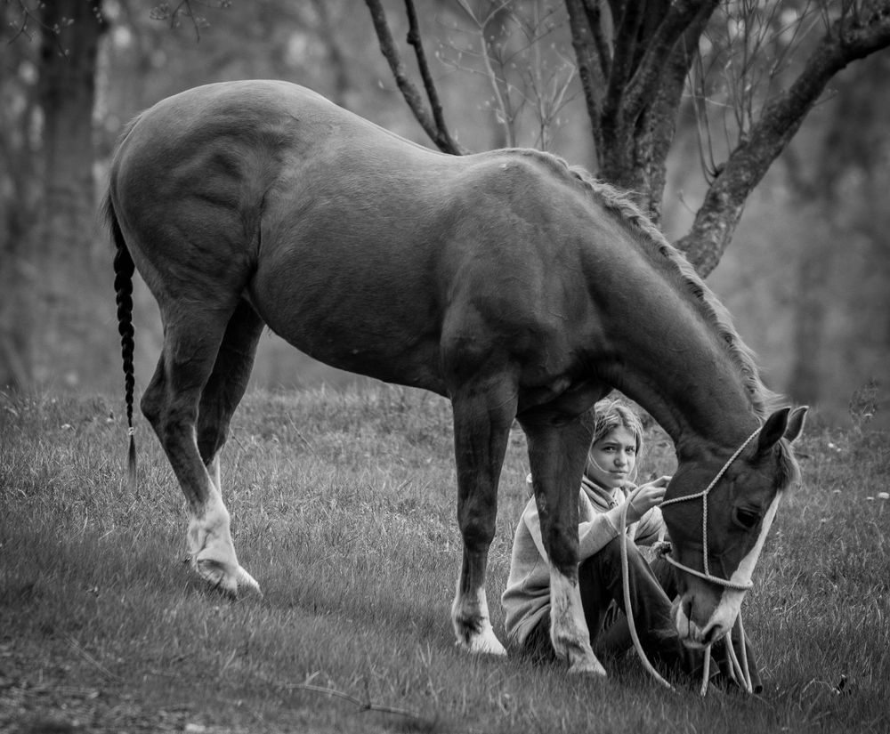 A black and white photo of a young girl sitting next to a horse.