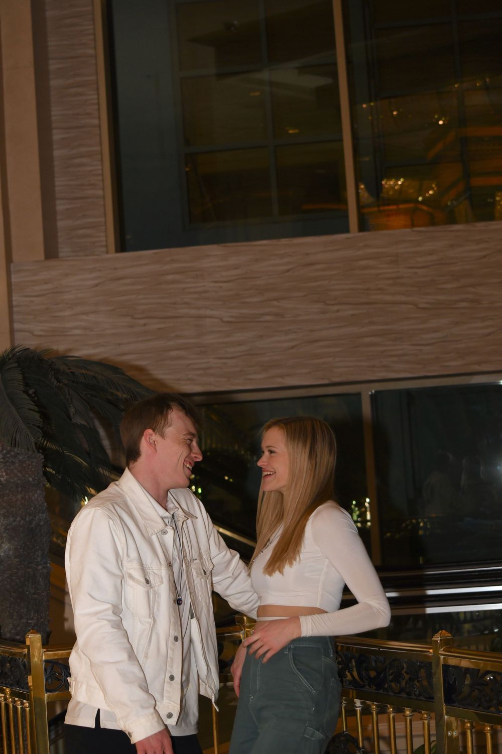 A couple in white outfits sharing a playful moment on a balcony at night.