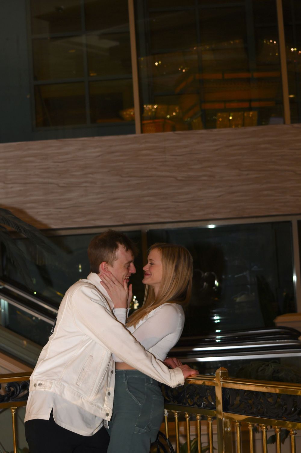 A romantic couple in white and denim sharing an intimate moment on a balcony at night.