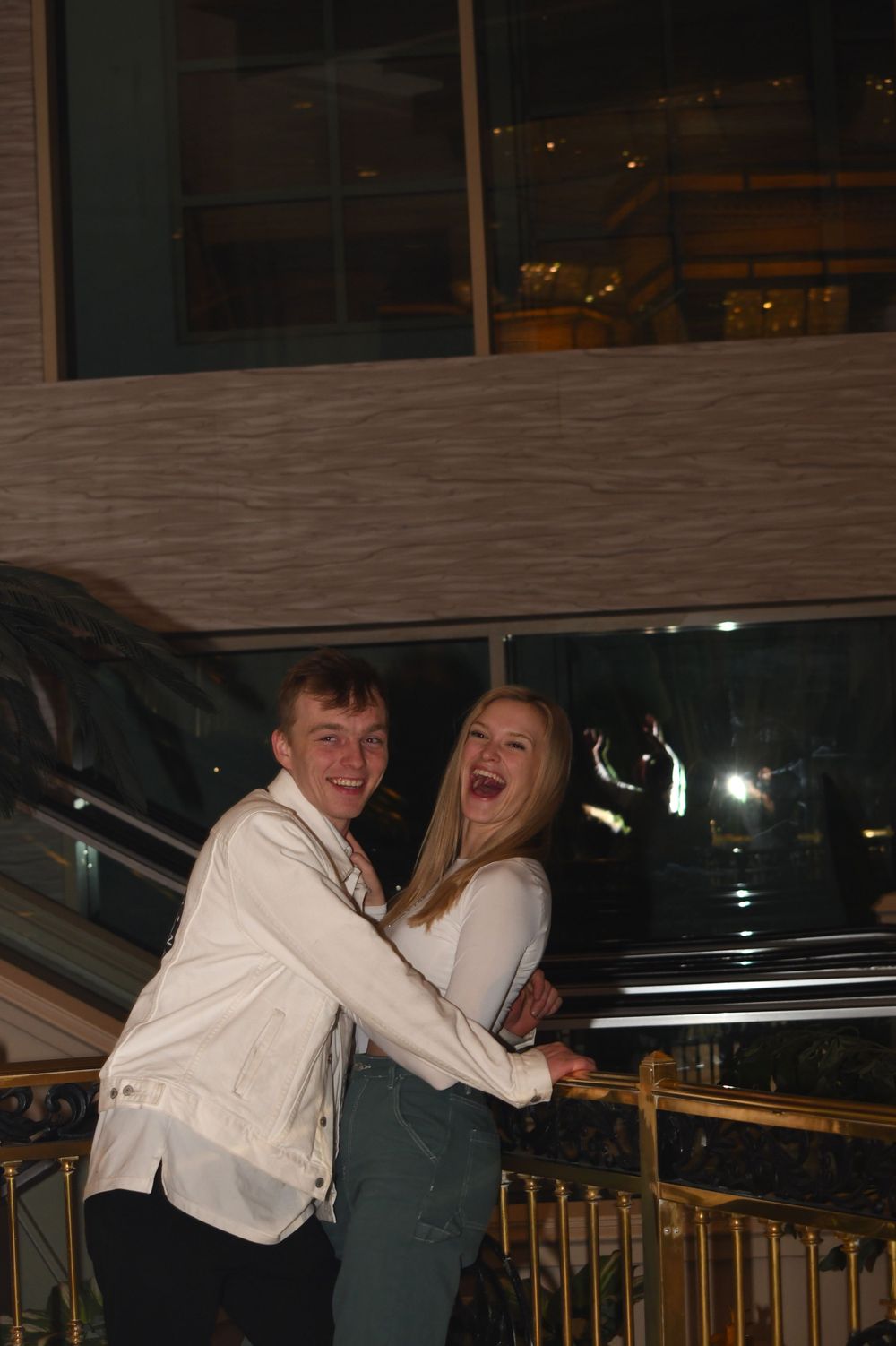 A joyful couple laughing while embracing on a balcony with nighttime city views.