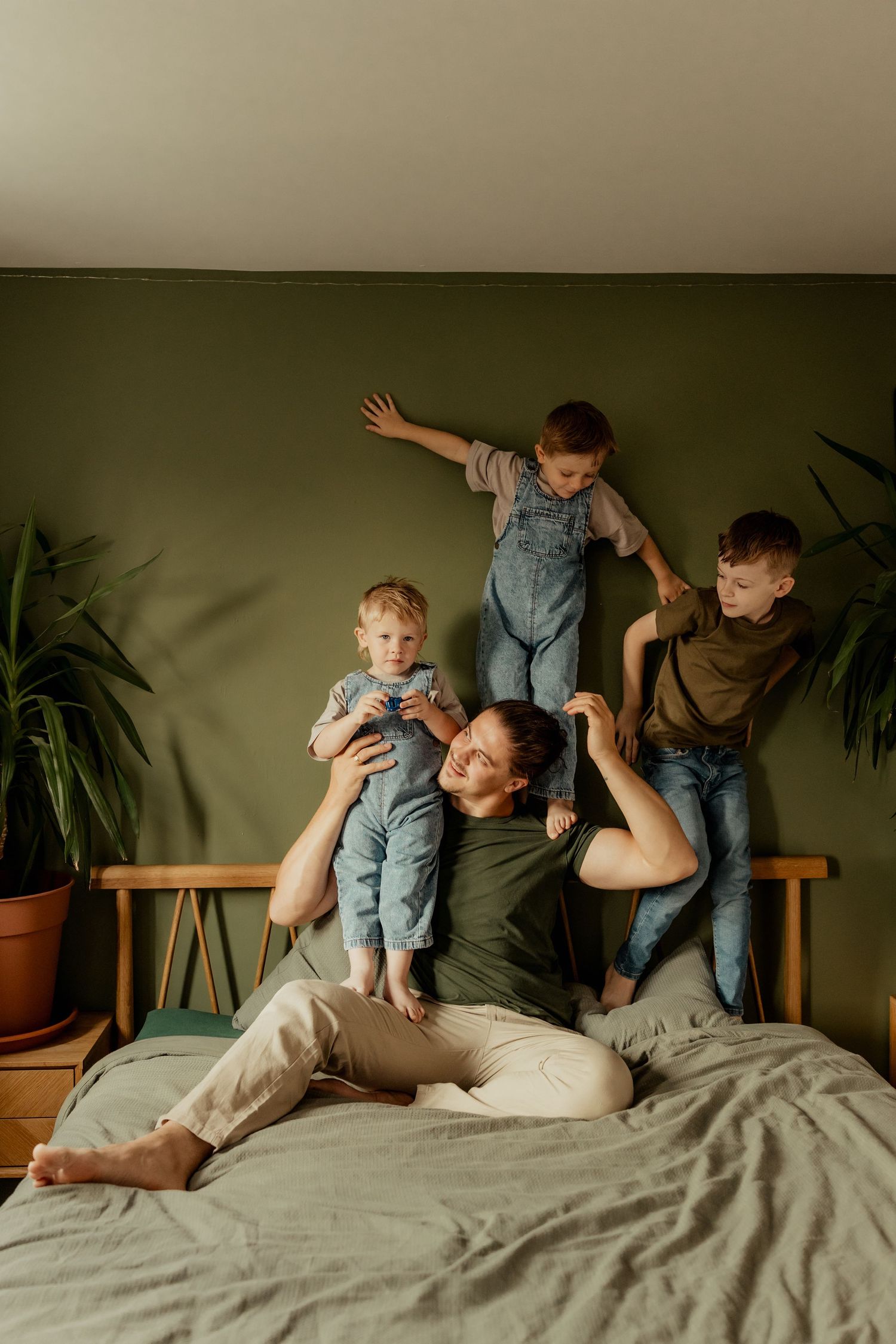 Adorable toddler in brown overalls crawls on bed while smiling with joy.