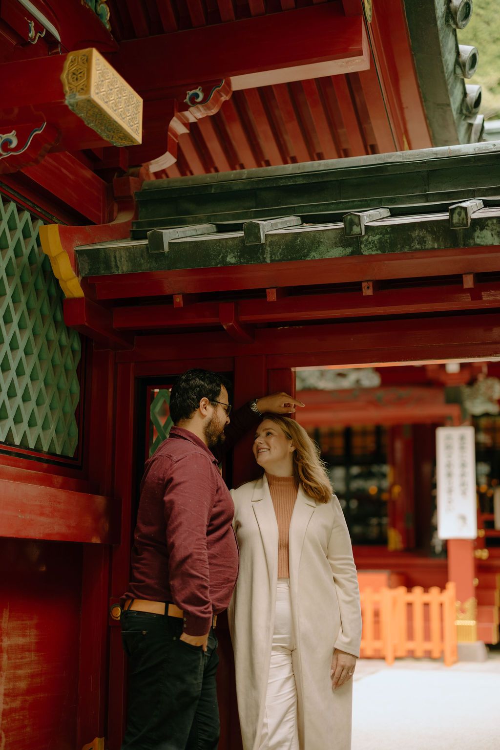 Couple sharing an intimate moment at a traditional Japanese shrine with red architecture.