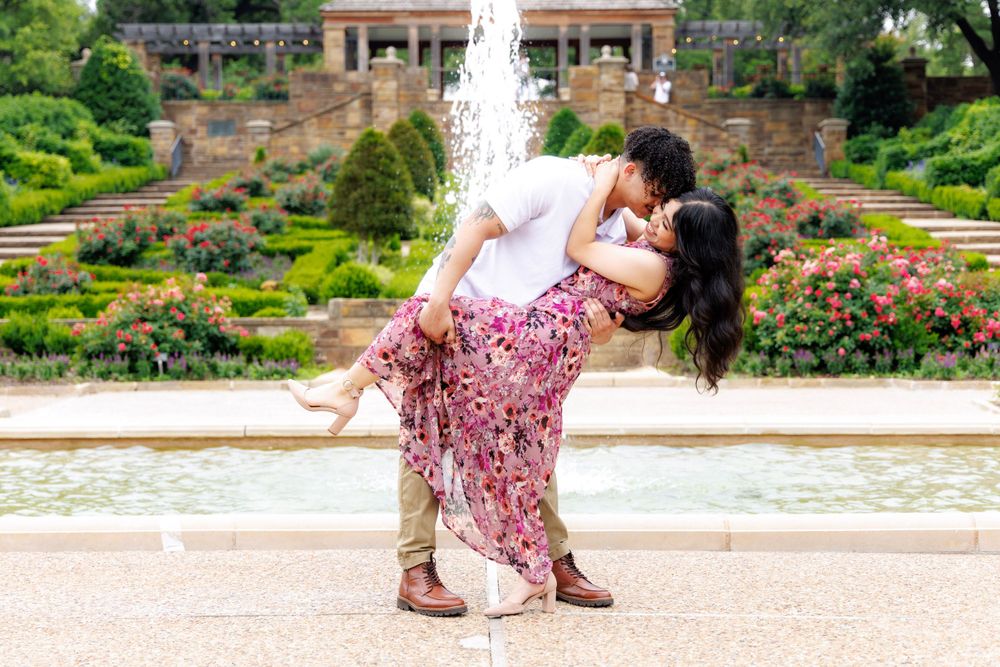 Romantic couple in floral dress sharing an intimate dance pose by a garden fountain.