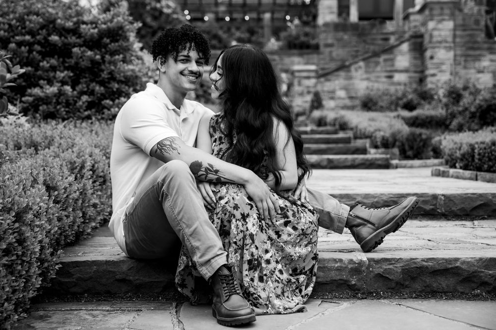 Black and white photo of couple sitting on stone steps in garden setting.