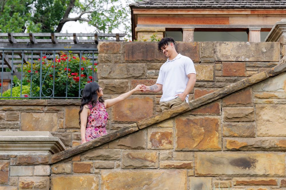 Couple holding hands while walking up stone stairs in garden setting.