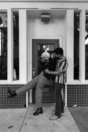 Two friends playfully posing in front of a white storefront entrance.