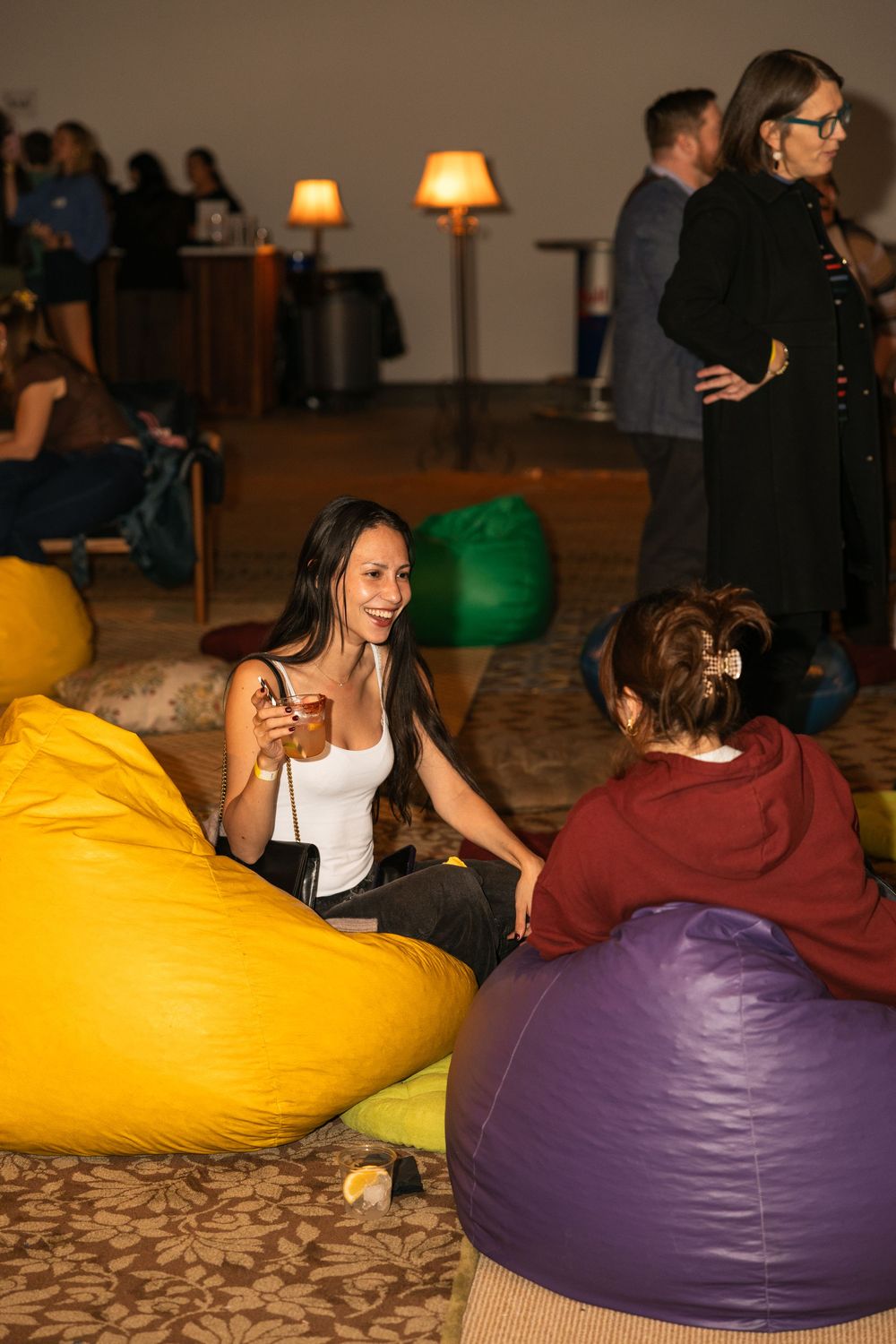 People relax on colorful bean bag chairs at an indoor social gathering with warm ambient lighting.
