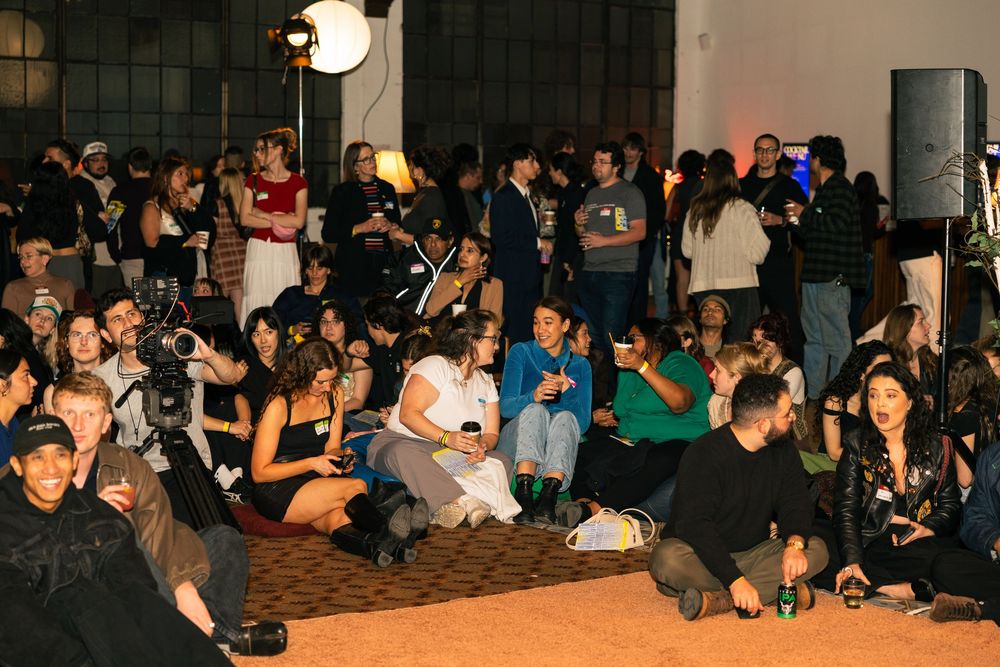 Large crowd seated in dark room during an indoor event or presentation.