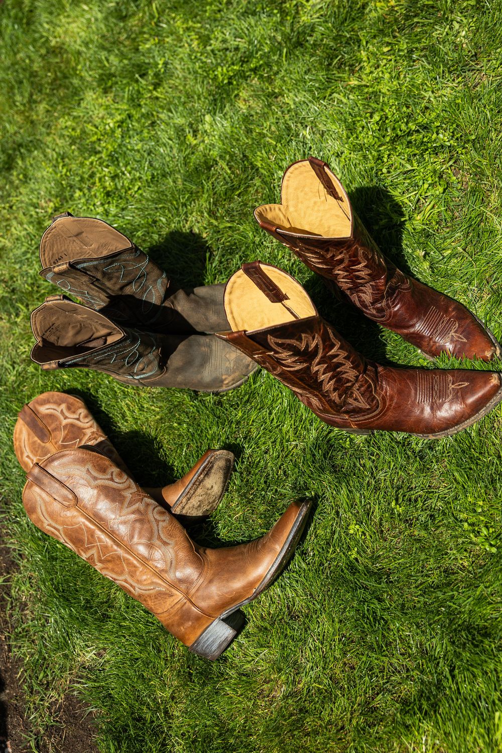 Two pairs of worn cowboy boots resting on green grass, one brown leather pair with boot shapers inserted.