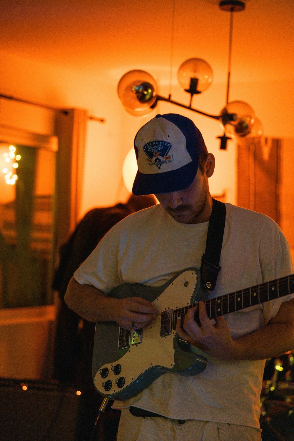 Musician playing electric bass guitar in warm orange lighting during a performance session.