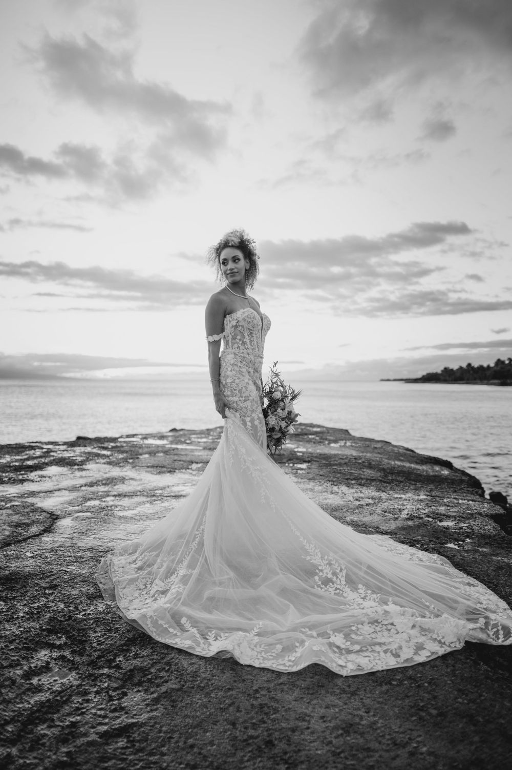A dramatic black and white wedding dress photo with flowing train against a coastal landscape.