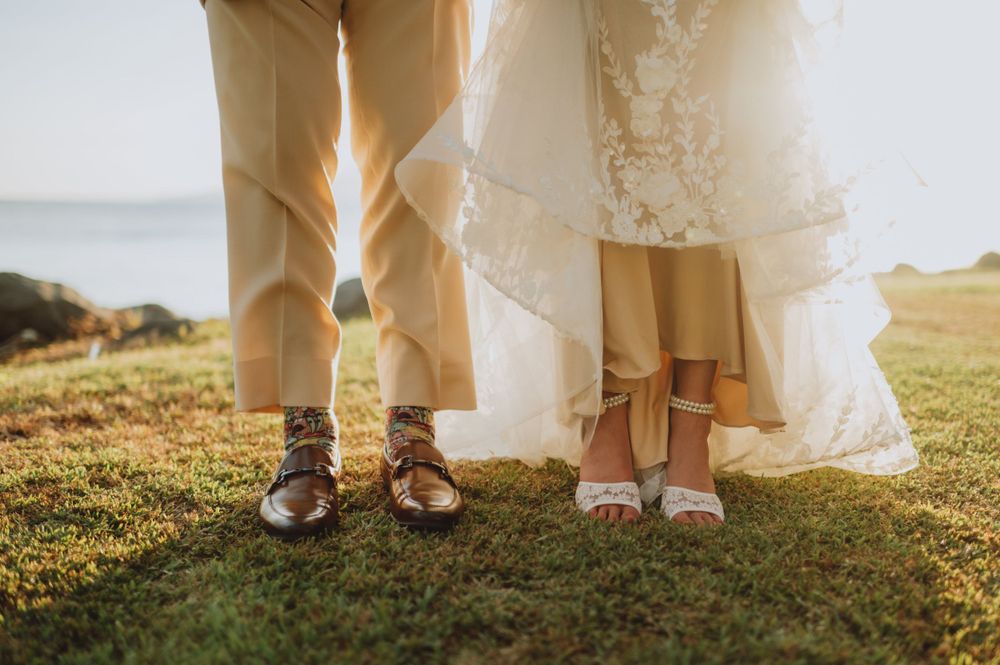 Close-up of bride and groom's feet on grass showing wedding shoes and dress hem.