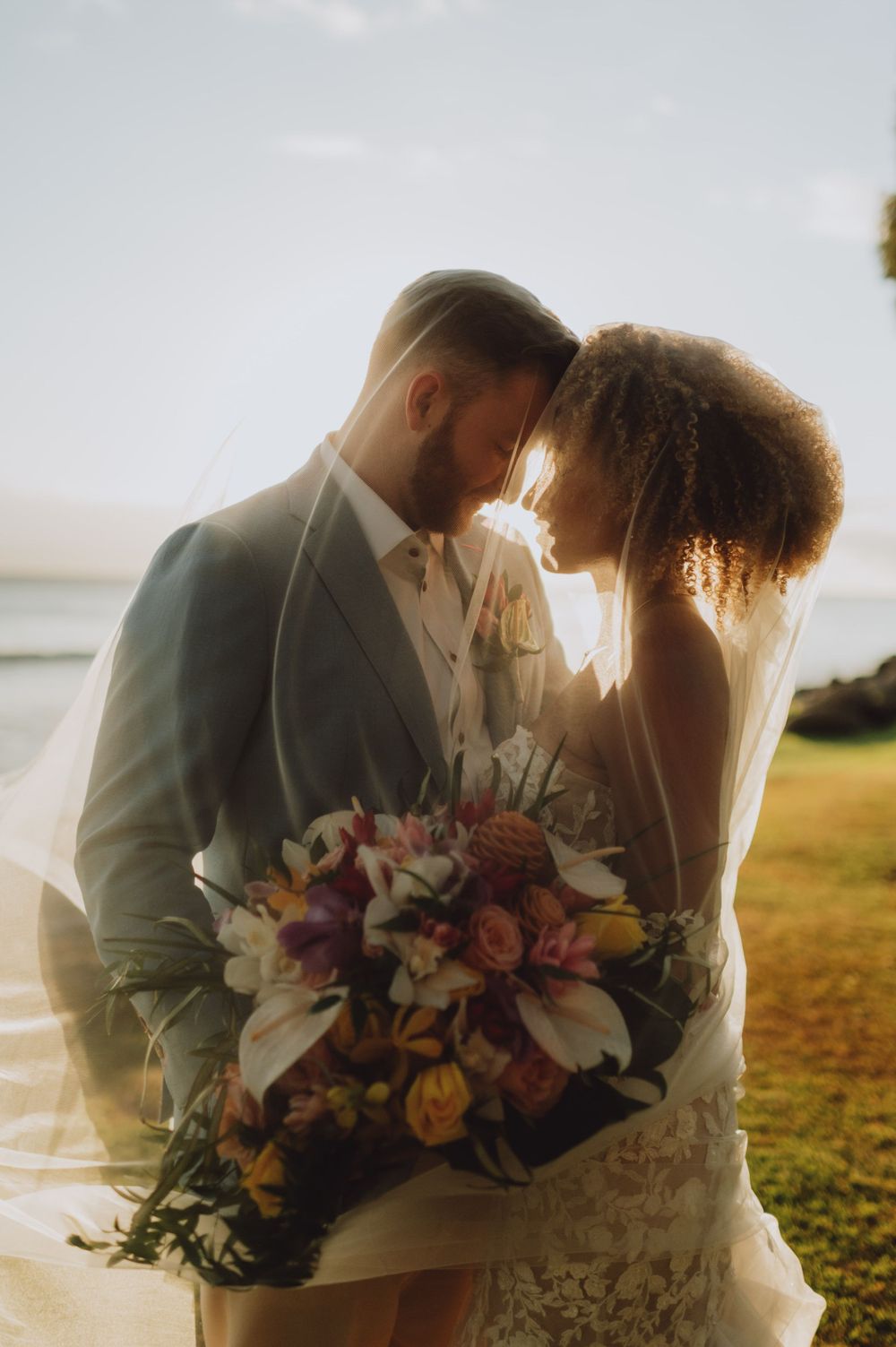 Wedding couple holding vibrant floral bouquet against golden sunset light.