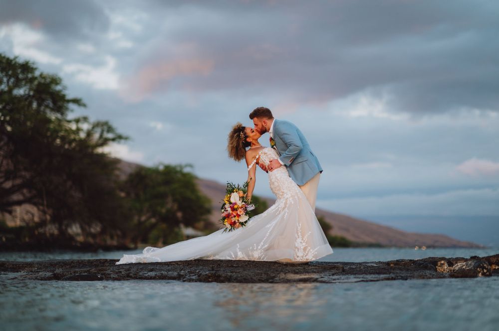 Dramatic cloudy sky frames wedding couple on Hawaiian beach at sunset.