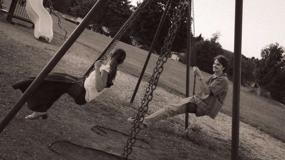 Two children playing on swings at a park playground in a vintage black and white photo.