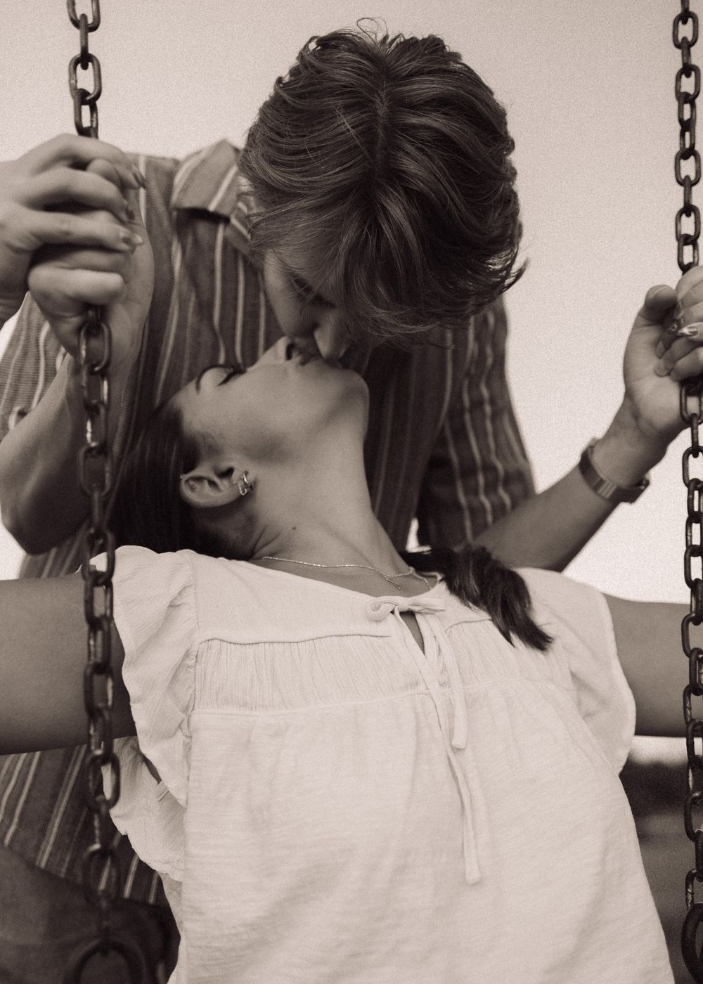 Romantic couple kissing on a swing set in a vintage black and white photo.