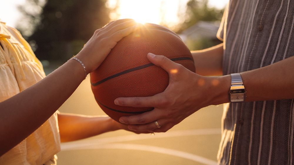 Two people sharing a basketball on an outdoor court bathed in warm golden sunlight.