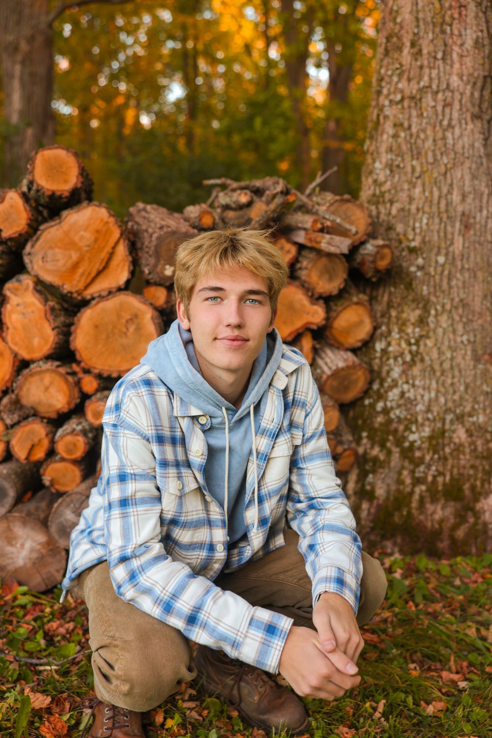 Senior session for boy posing by a wood pile.
