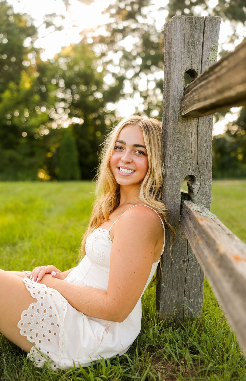 Senior portrait beautiful lighting at a park leaning on a fence.