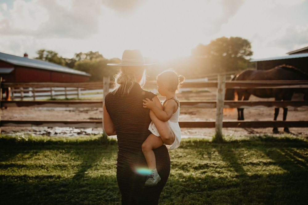 Silhouetted couple embracing in a sunlit field with wooden fences and golden hour lighting.