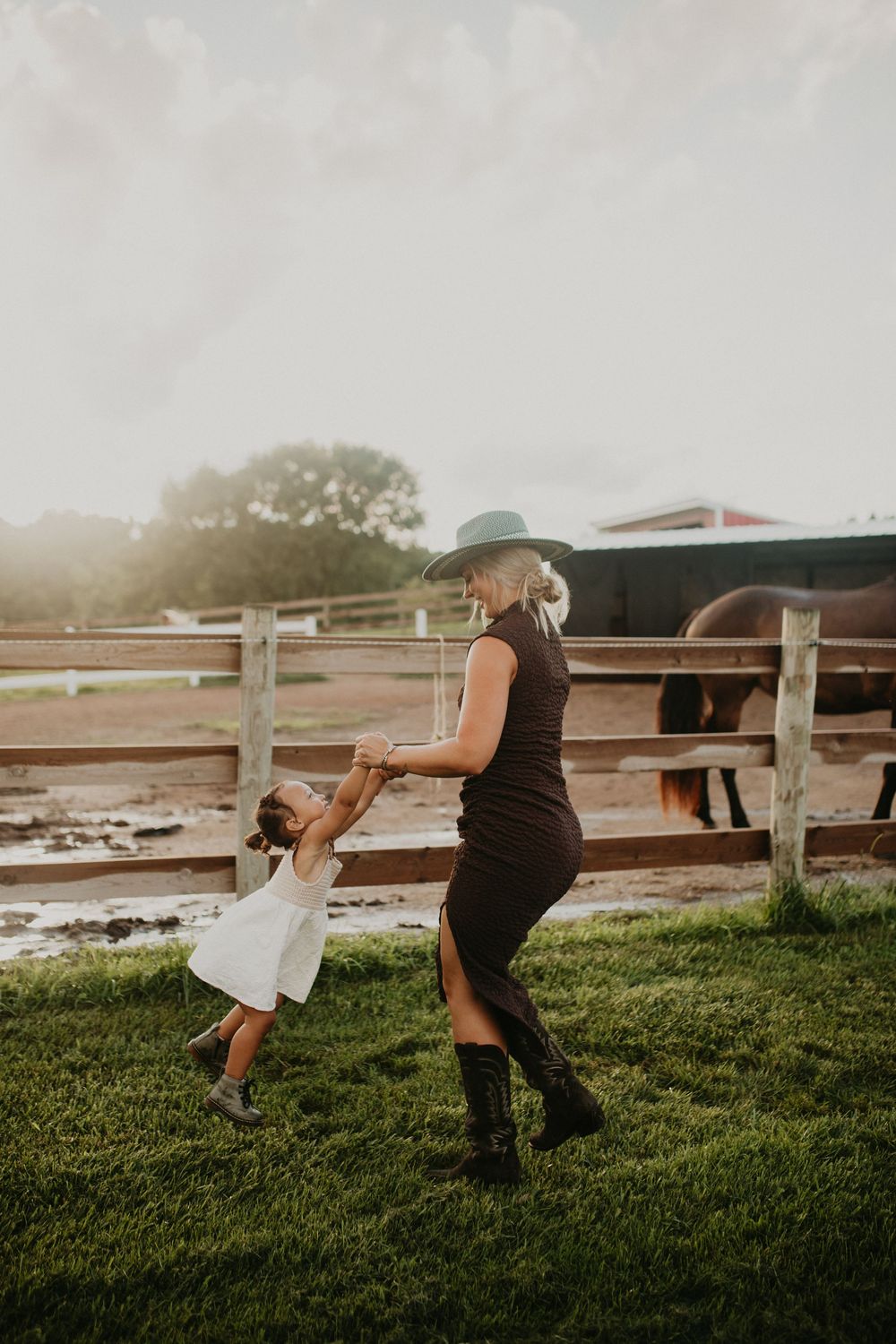 Two people play together on a grassy field near a white fence during golden hour.