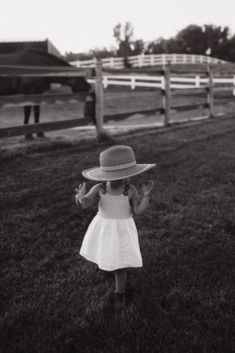 Black and white photo series of a small child in a sunhat playing in a grassy field with white fencing in background.