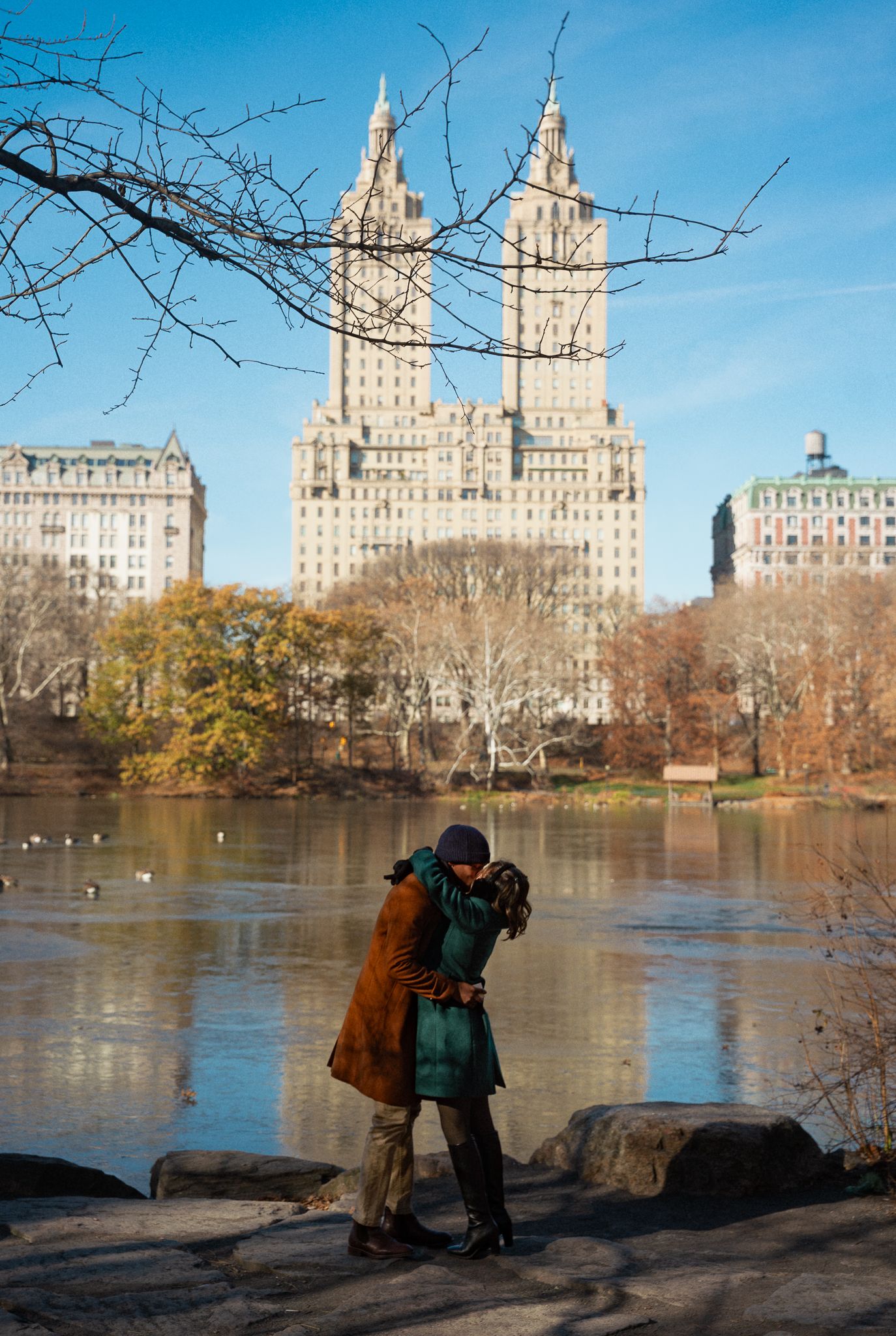 A winter scene at Central Park with iconic buildings reflecting in the lake.