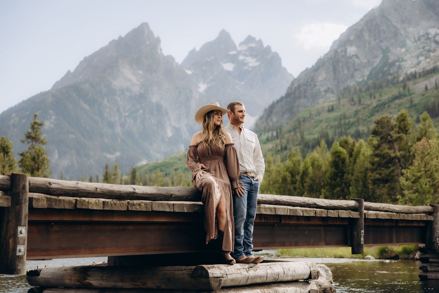 Close-up view of hands embracing from behind with engagement ring visible against mountain landscape backdrop.