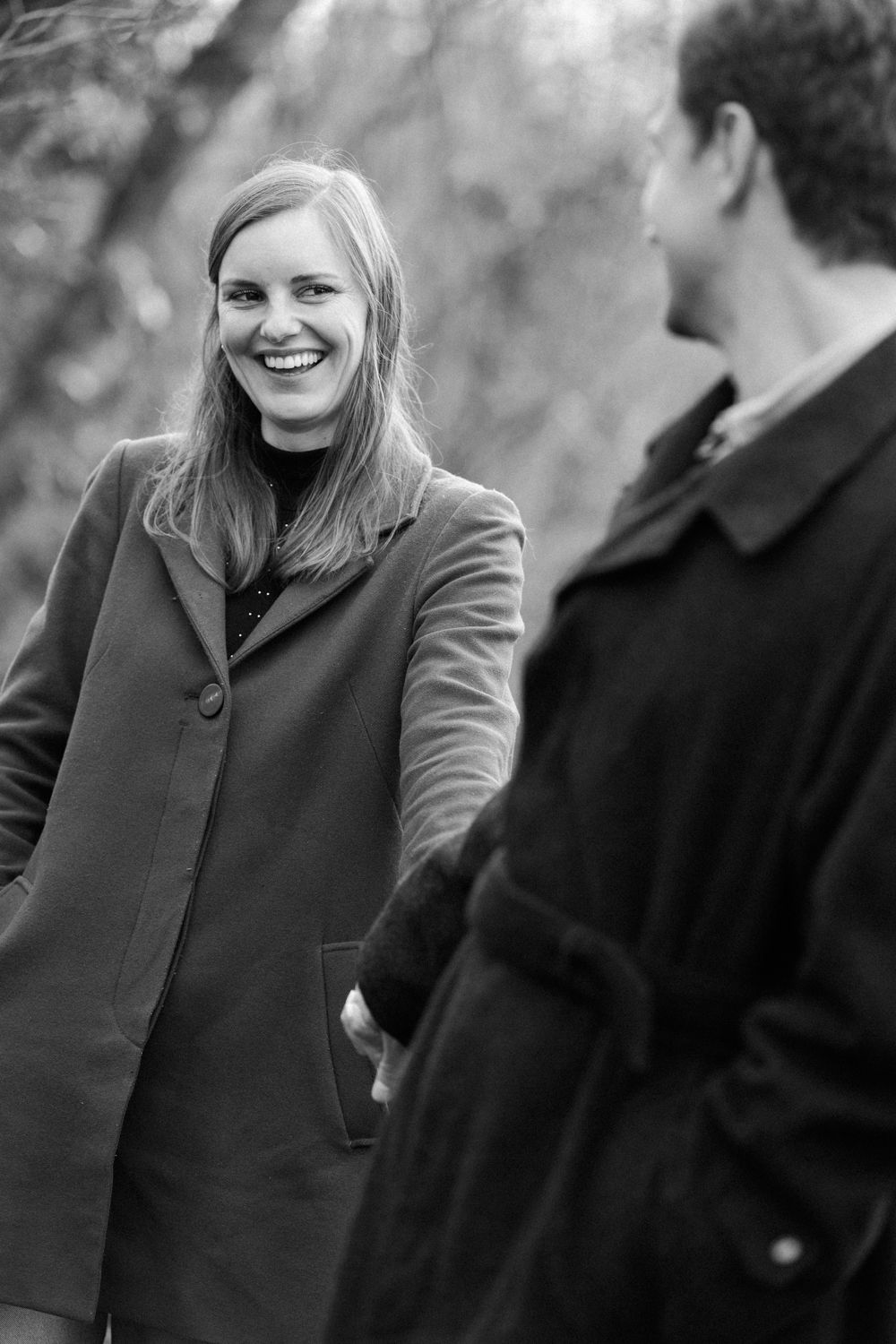 A series of black and white photos showing someone in a gray coat smiling and interacting with others outdoors.