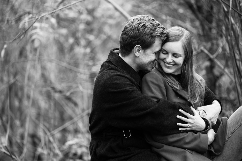 A couple shares an intimate embrace in a black and white outdoor setting surrounded by trees.