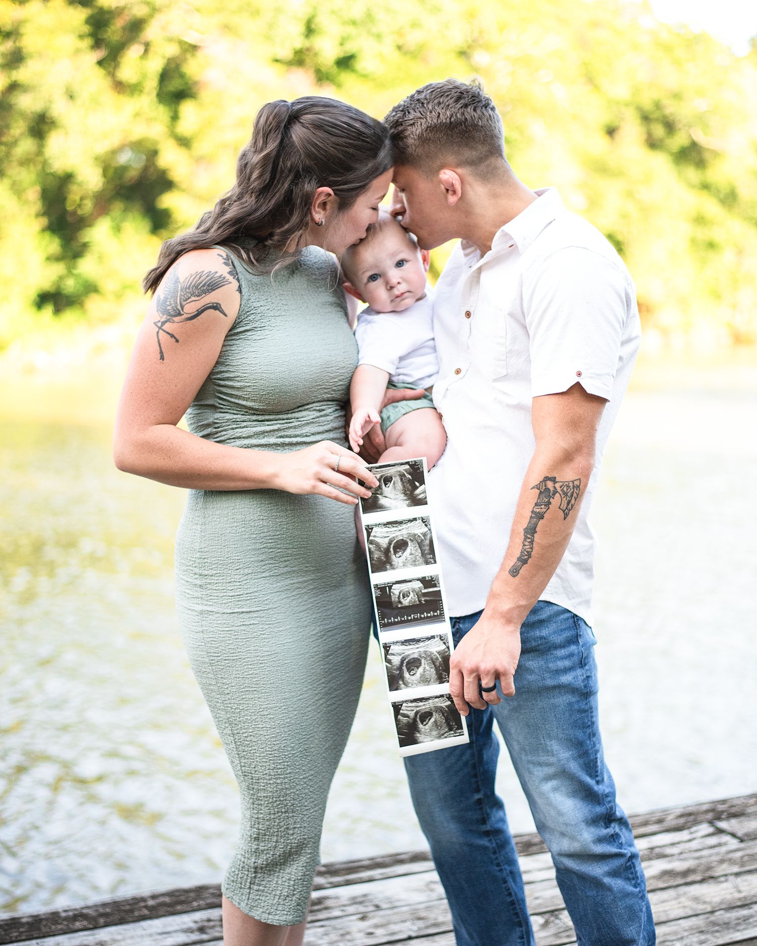 Expecting couple holding ultrasound photos and their baby outdoors near a lake announcing a pregnancy.
