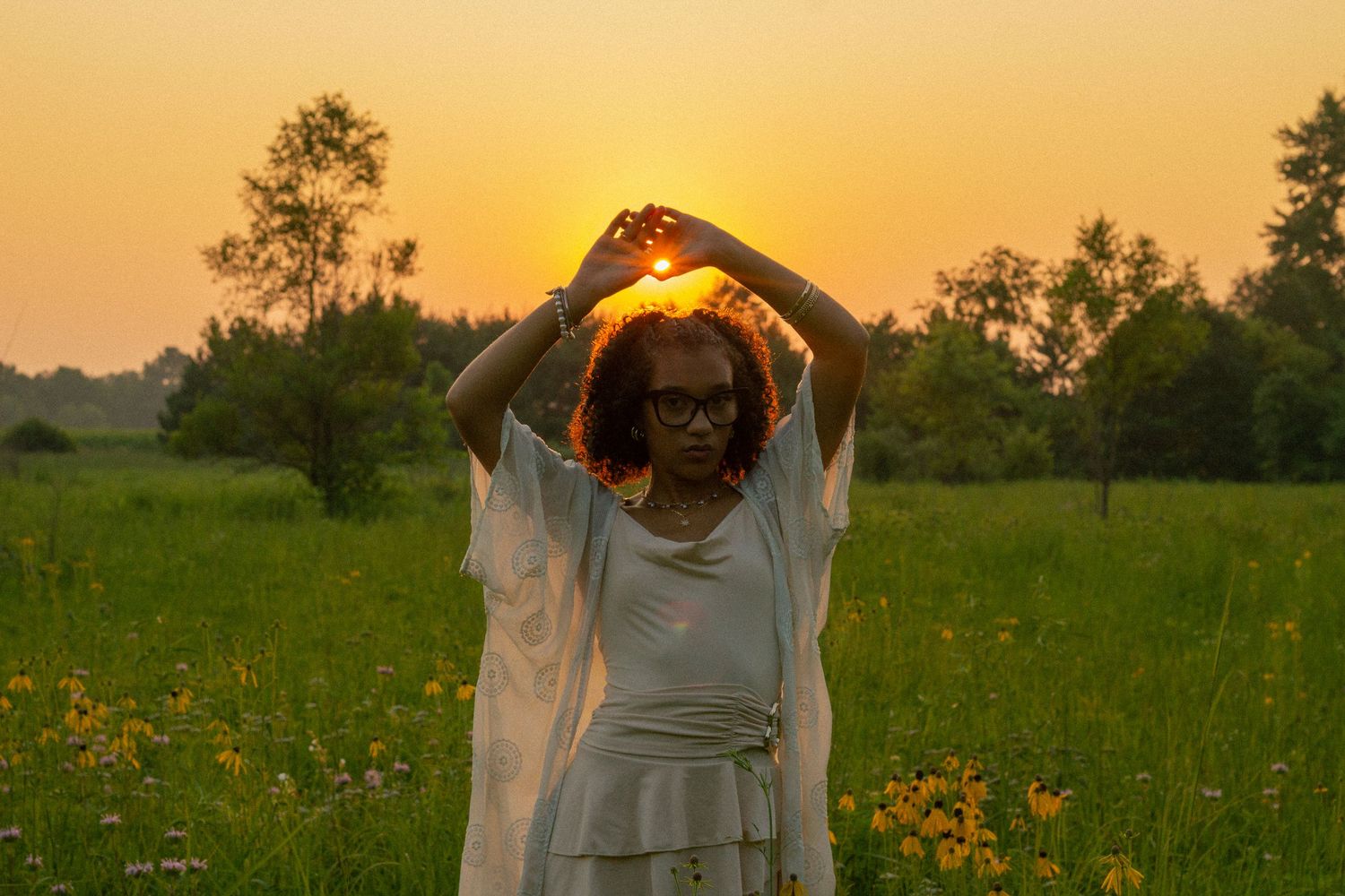 A person in a white flowing dress dances joyfully in a wildflower meadow at golden hour during her senior photo session in Michigan.