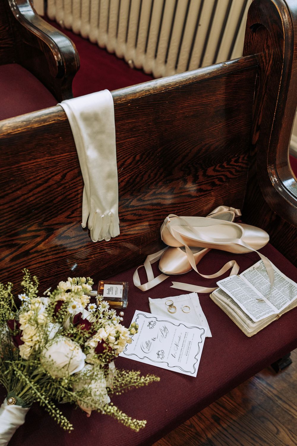 Bridal details including satin shoes, gloves, bouquet, and rings on church pew.