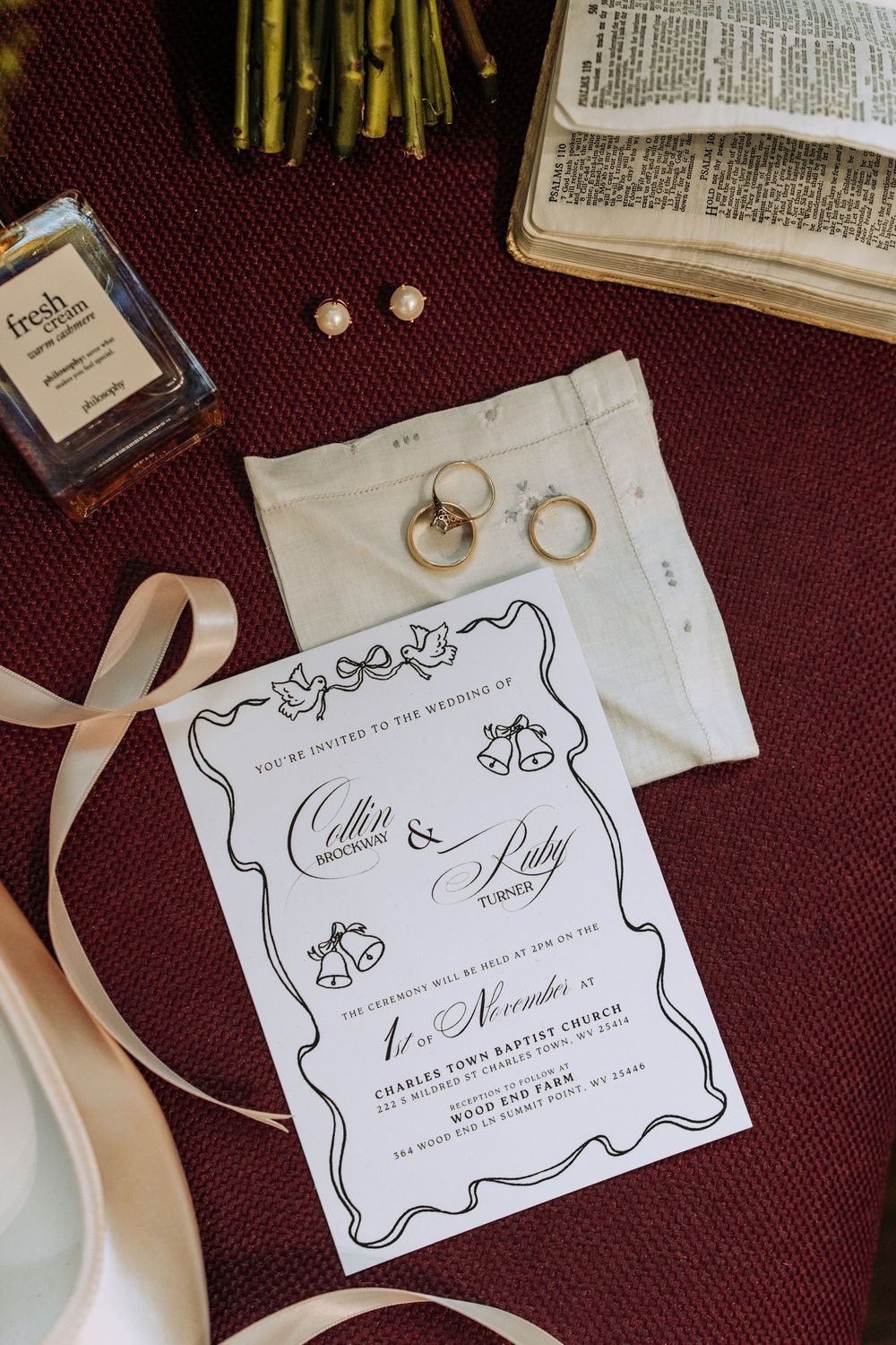 Wedding flat lay featuring invitation for Cullen and Ruby, gold rings, and perfume.