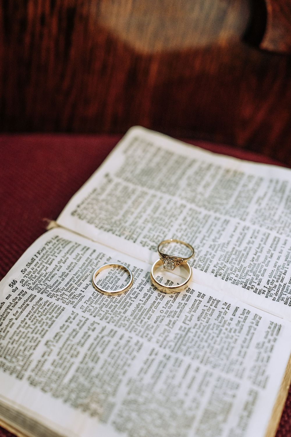 Two gold wedding rings resting on open Bible pages on church pew.