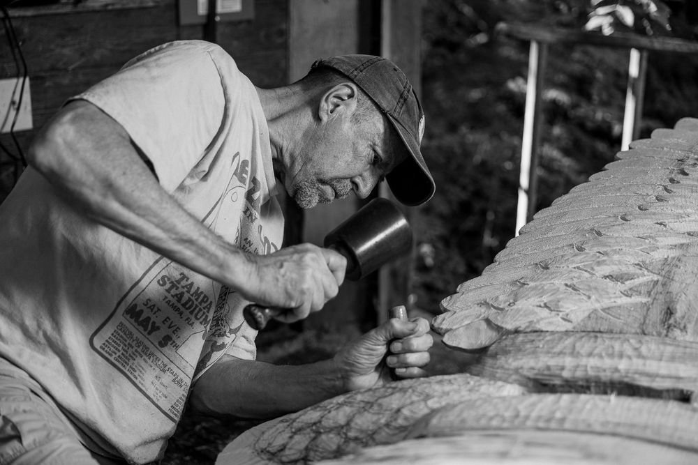 A craftsperson carefully carves intricate details into a stone sculpture using specialized tools.