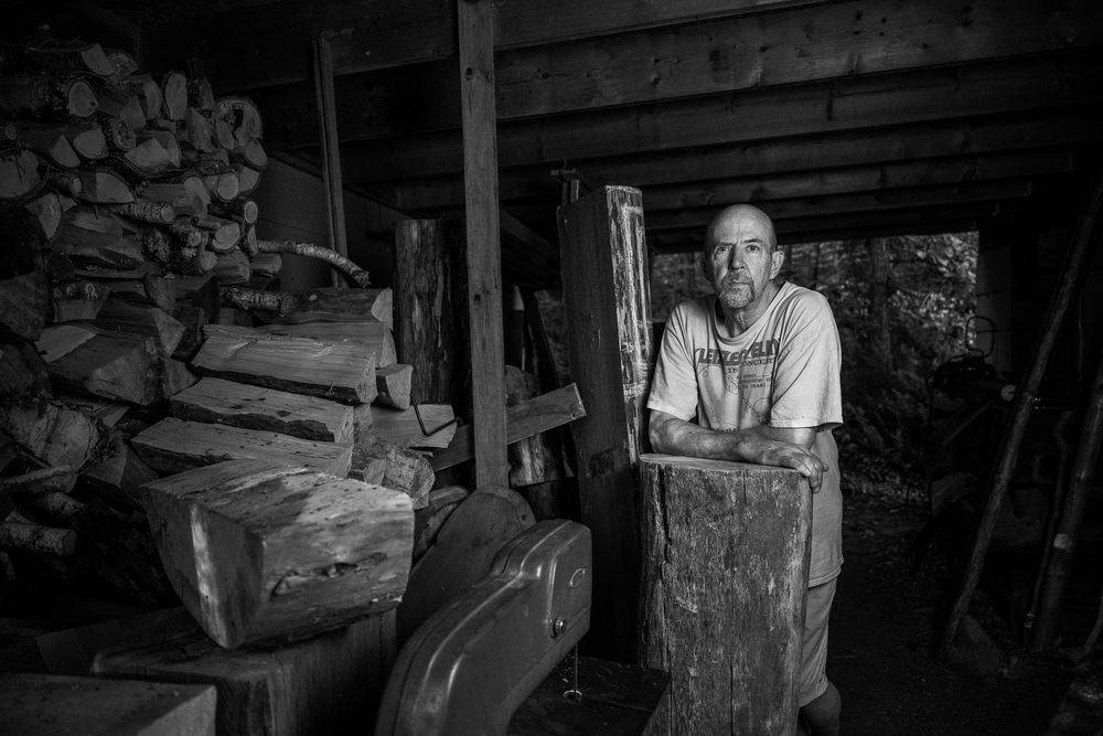 A panoramic black and white image showing someone working in a traditional woodshop with stone walls and tools.