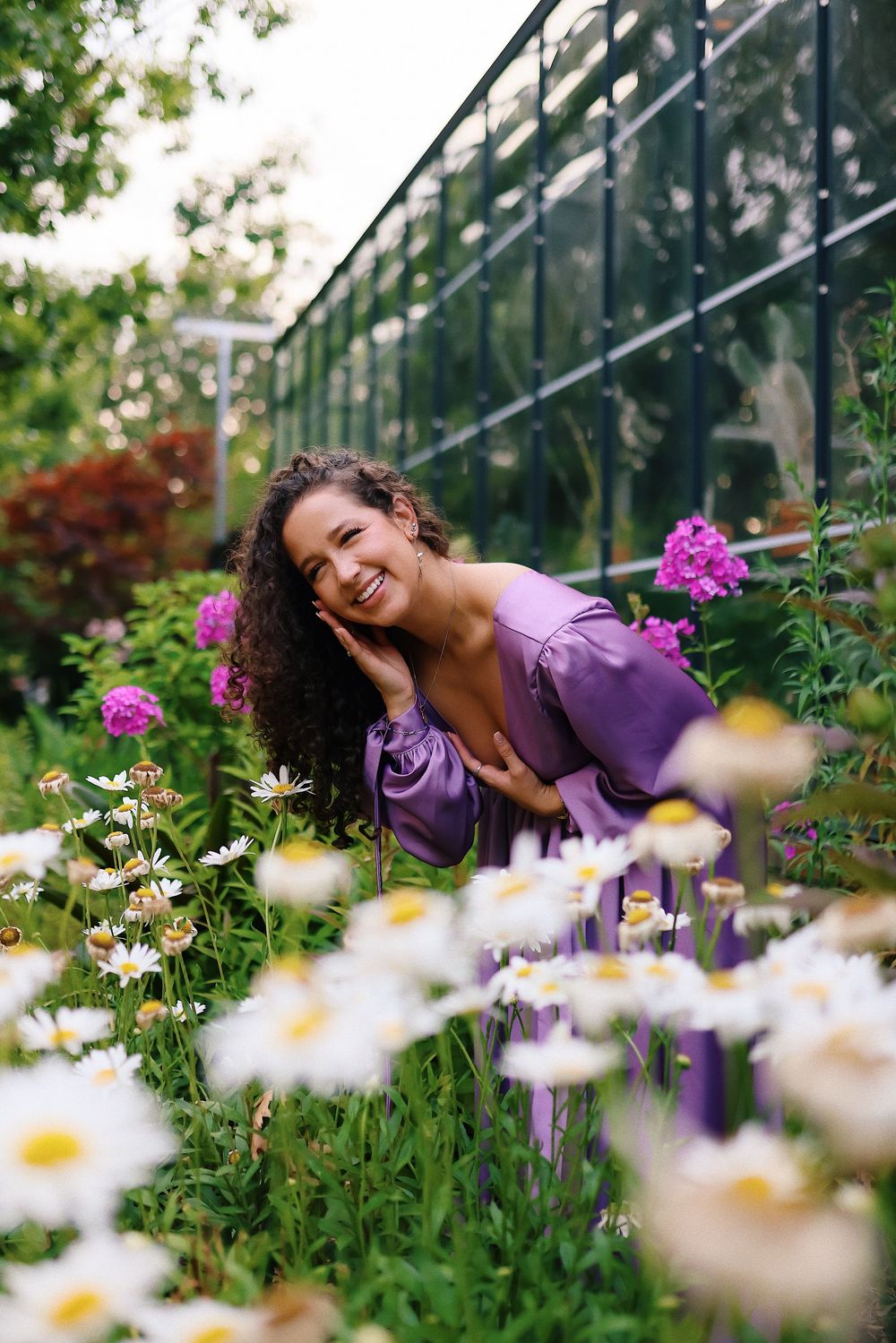 A series of dreamy photos showing someone in a purple top laying among blooming daisies and pink flowers in a garden.