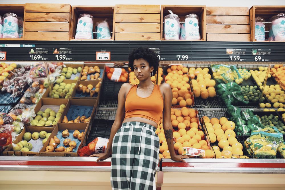 Fresh produce and vegetables displayed in well-stocked grocery store shelves with bright lighting and wooden wall decor.