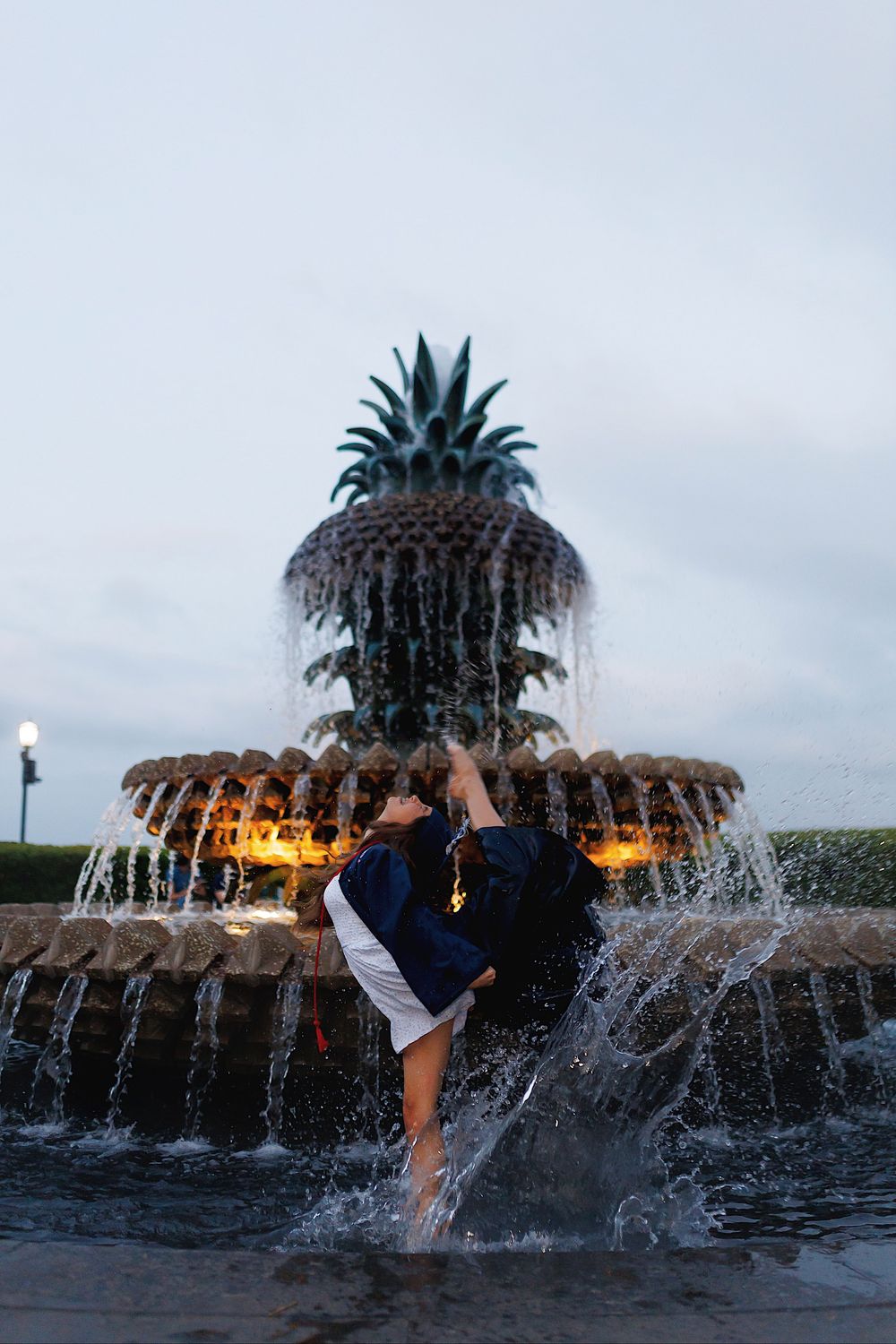 A couple embraces in front of the illuminated Pineapple Fountain at Waterfront Park in Charleston at dusk.