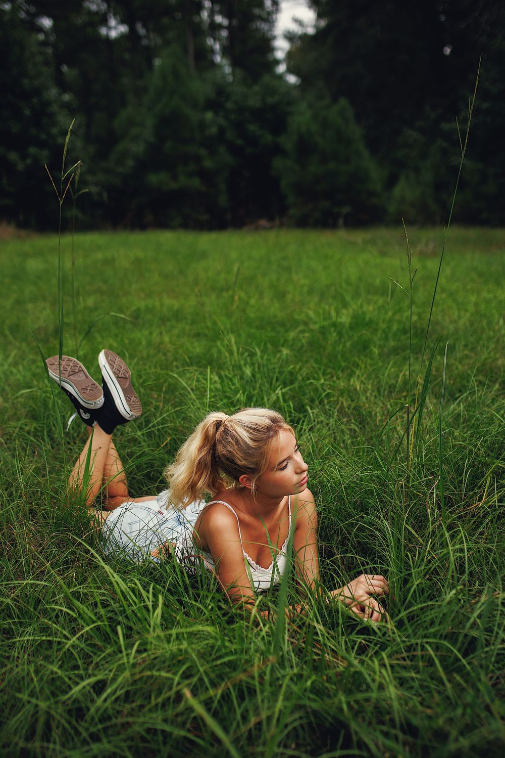 Person in a floral dress lying peacefully in tall green grass on a summer day.